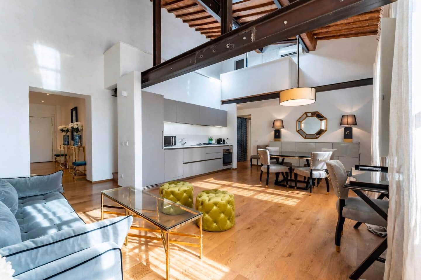 At Home — spazio open space luminoso per soggiorno e pranzo sotto un soffitto a travi a doppia altezza, con divano azzurro