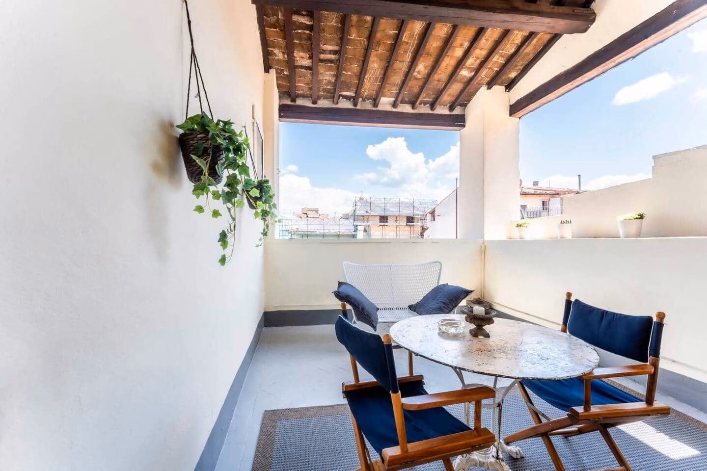 Loggia — loggia coperta sul tetto con tavolino da bistrot in marmo e sedie blu affacciata sui tetti di Firenze