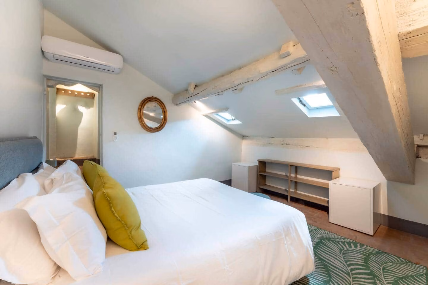 Loggia — camera mansardata con soffitto spiovente imbiancato, travi a vista, due lucernari e letto matrimoniale in lino bianco