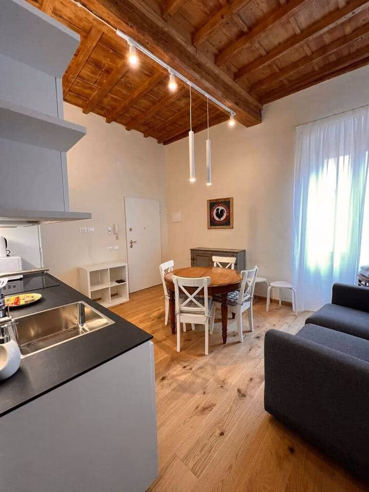 Sprone Right — soggiorno e sala da pranzo open space con soffitto a travi a vista, pavimenti in rovere, tavolo rotondo e divano grigio