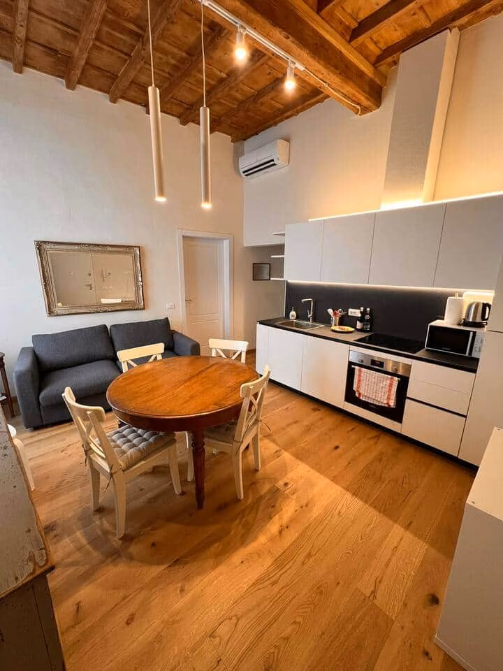 Sprone Right — cucina bianca attrezzata con forno e piano cottura accanto a un tavolo rotondo sotto soffitti a travi